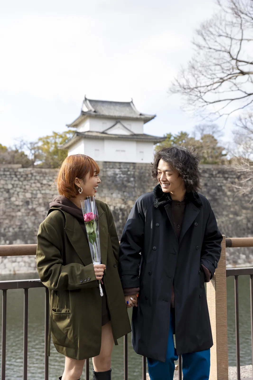 Two people talking outdoors beside a castle wall